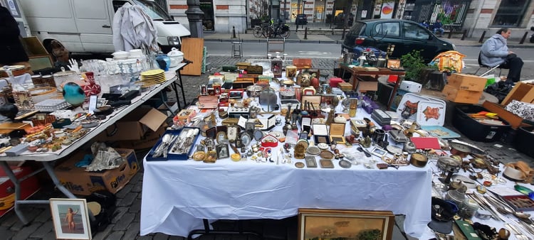 Rommelmarktkraam in Brussel: zilverwerk, klokken, schilderijen en antiek uitgestald op tafels.