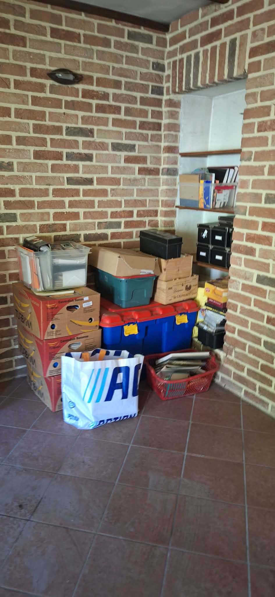 Hoek van de woonkamer na het sorteren: kisten, bakken en mappen netjes opgestapeld tegen een bakstenen muur.