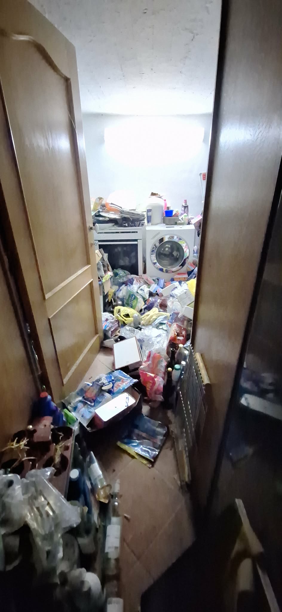 Onbereikbaar geworden wasplaats, gezien vanaf de deur: zakken, verpakkingen en producten opgestapeld tot aan de wasmachine.