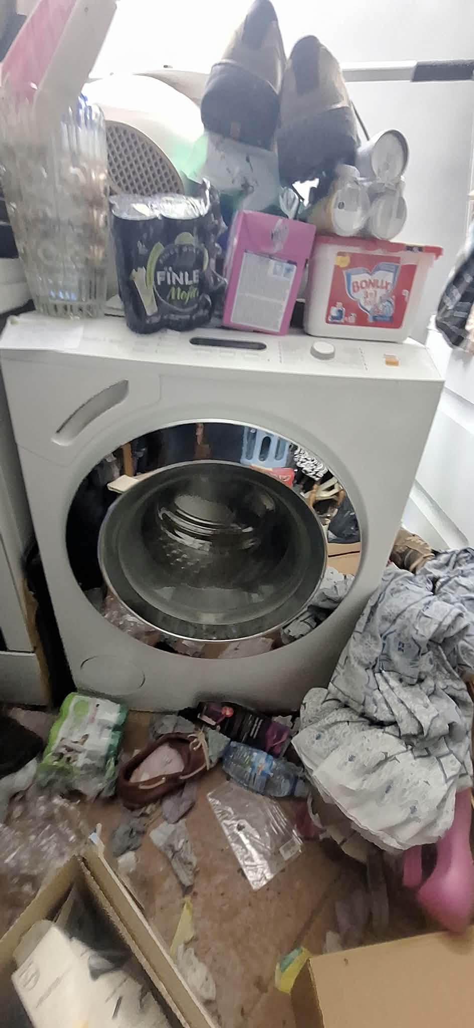 Wasmachine omringd door spullen, was en verpakkingen in een te ontruimen wasplaats.