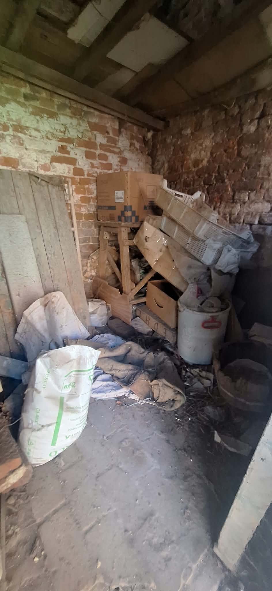 Bakstenen bijgebouw dat leeggemaakt moet worden: zakken, houten kisten en bakken op een aarden vloer.